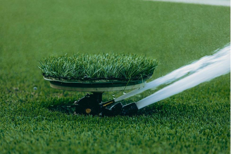 Close-up of an efficient sprinkler head spraying water and camouflaged to blend in with the surrounding green grass.