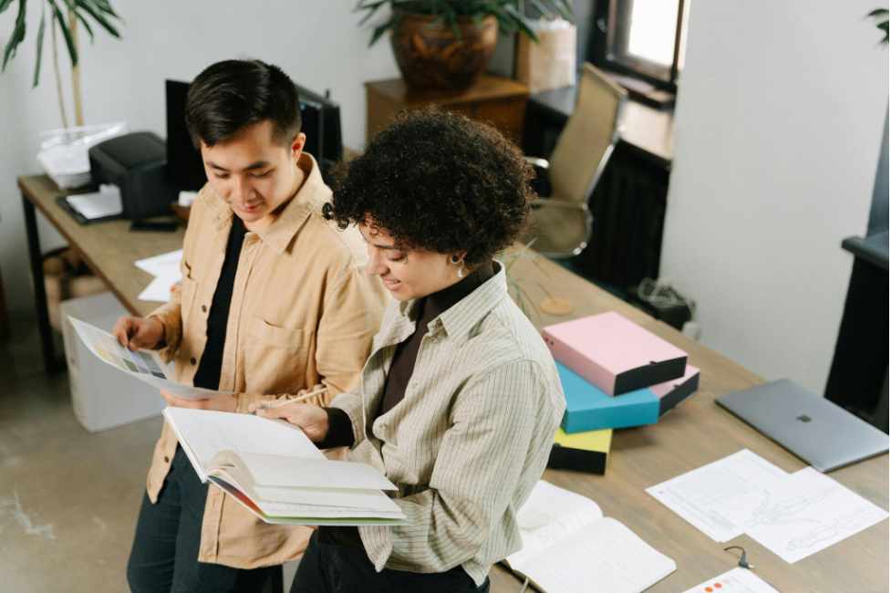 Two smiling people leaning on a desk and reviewing documents together