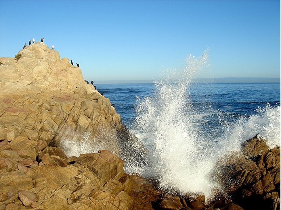 A wave crashing into the rocky California shoreline.