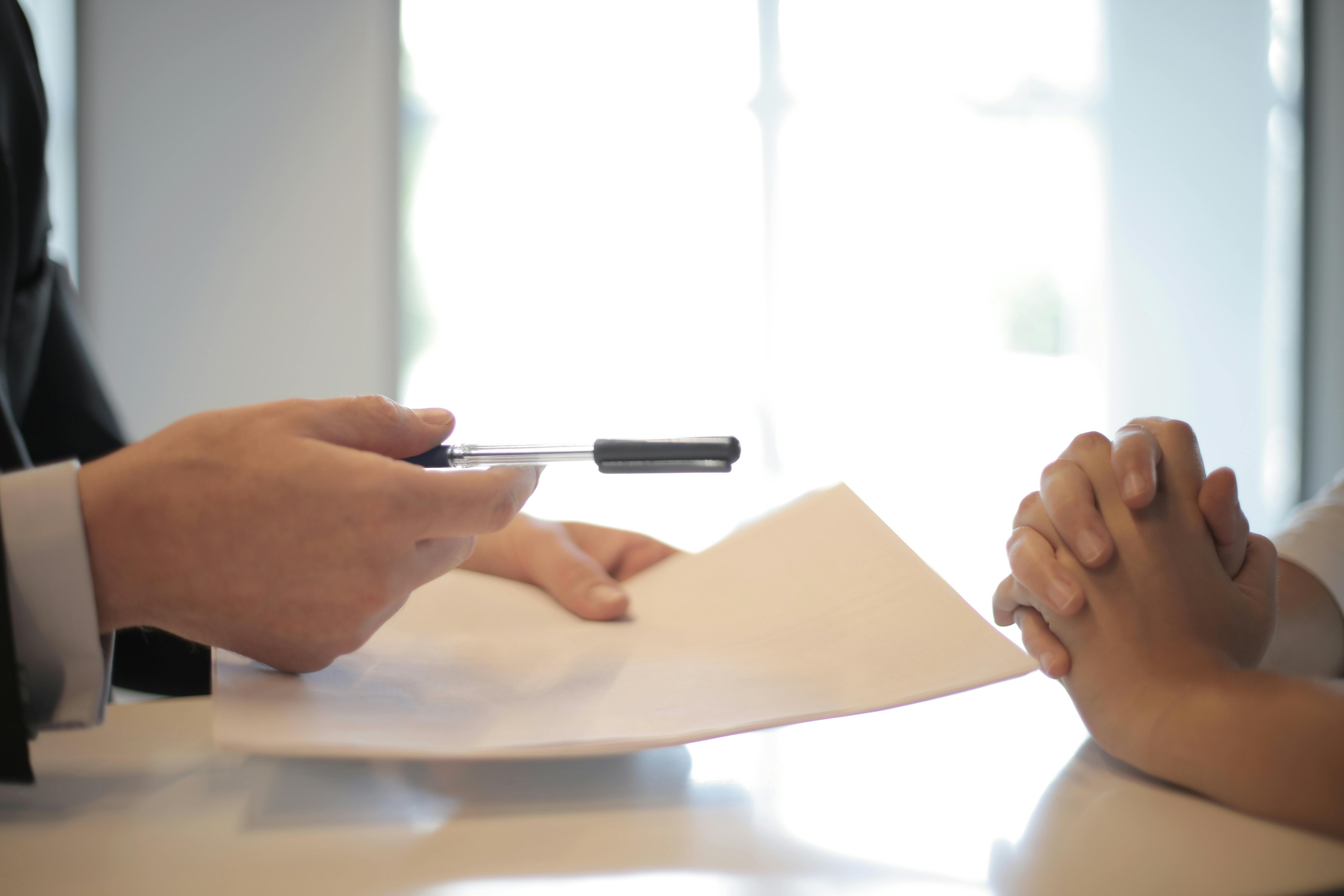 someone handing over paper and pen to someone else