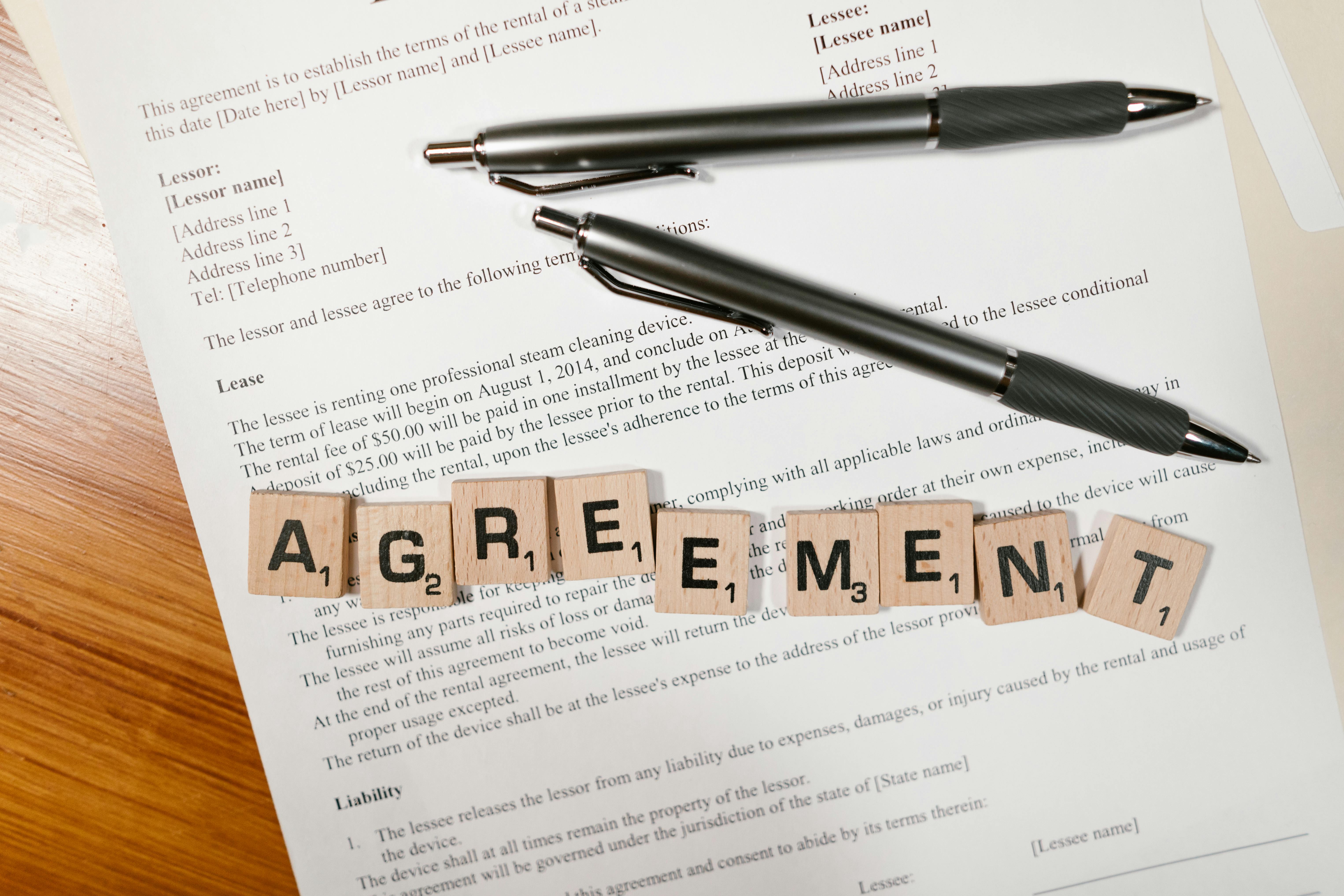 lease agreement with two black pens on top and Scrabble tiles spelling out the word 