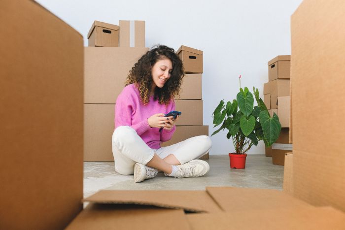Cheerful woman checking phone surrounded by moving boxes indoors