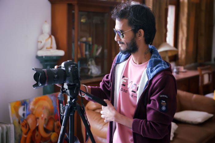 Man adjusting a DSLR camera on a tripod in a cozy indoor setting