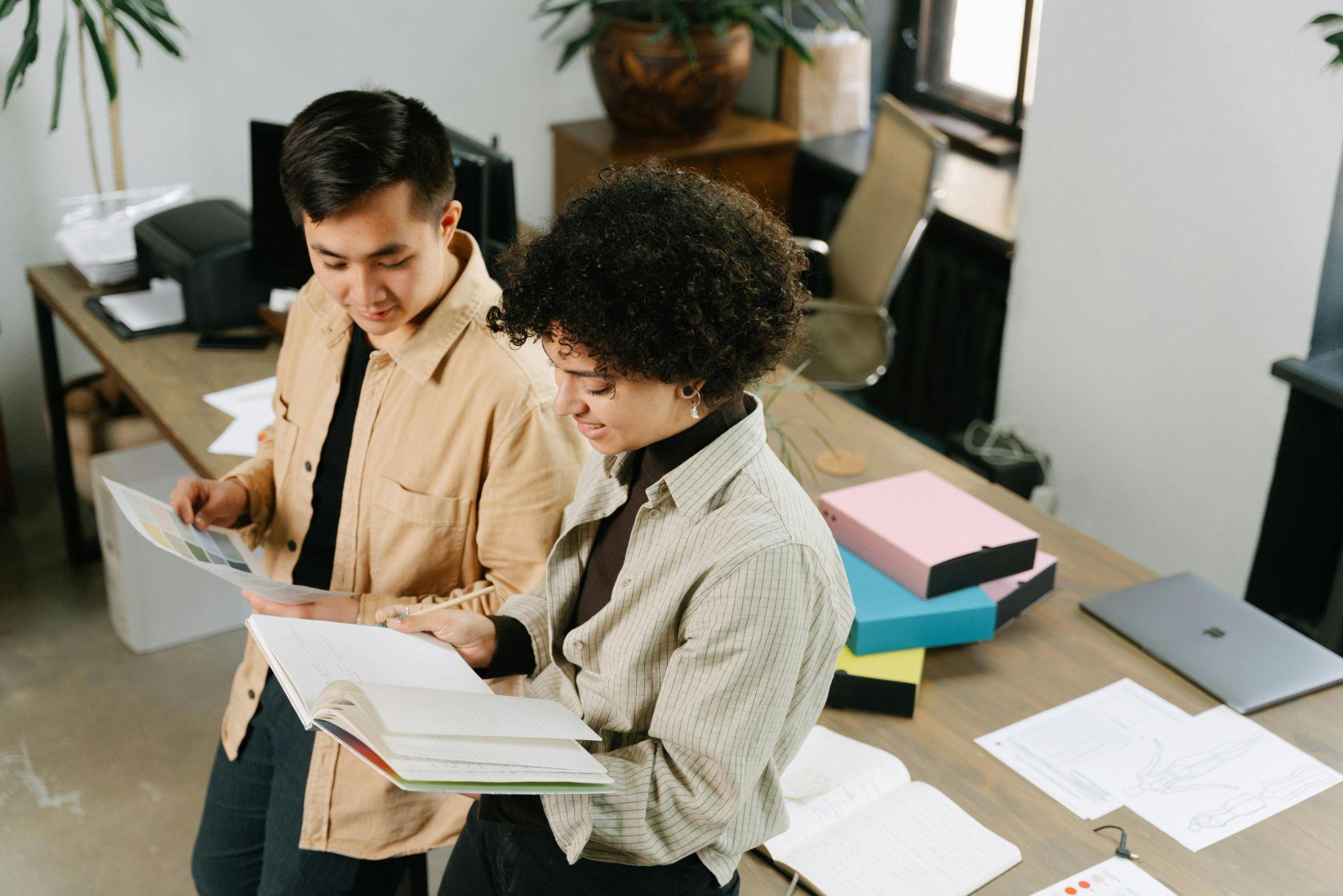 Two smiling professionals leaning on a desk and discussing paperwork