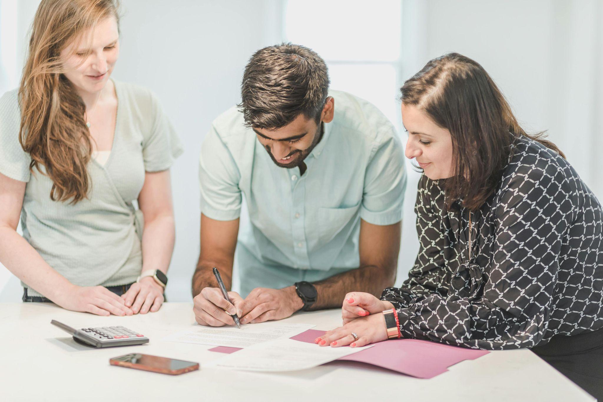 A person signing a contract while two other people stand on either side of him